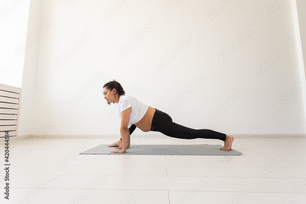 Fototapeta premium Purposeful pregnant woman exercises during yoga class and relaxes while sitting on a mat on the floor. Concept of physical and mental preparation of the body for childbirth. Place for text