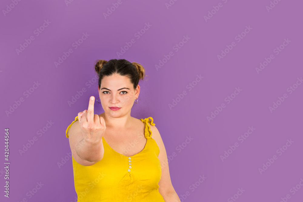 Mujer joven con la mano levantada mostrando un solo dedo medio levantado en gesto grosero sobre un fondo morado liso y aislado. Vista de frente. Copy space Mujer joven con la mano levantada mostrando un solo dedo medio levantado en gesto grosero sobre un fondo morado liso y aislado. Vista de frente. Copy space