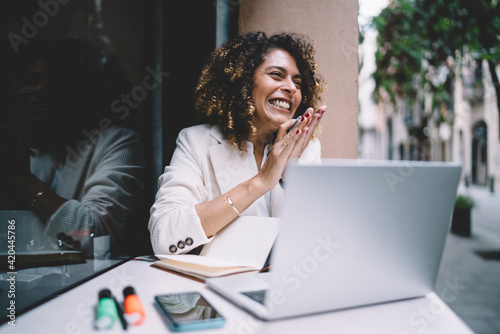 Cheerful female graphic designer feeling delight and happiness while doing remote work on laptop computer rejoicing at sidewalk cafe, joyful woman with netbook satisfied with freelance lifestyle