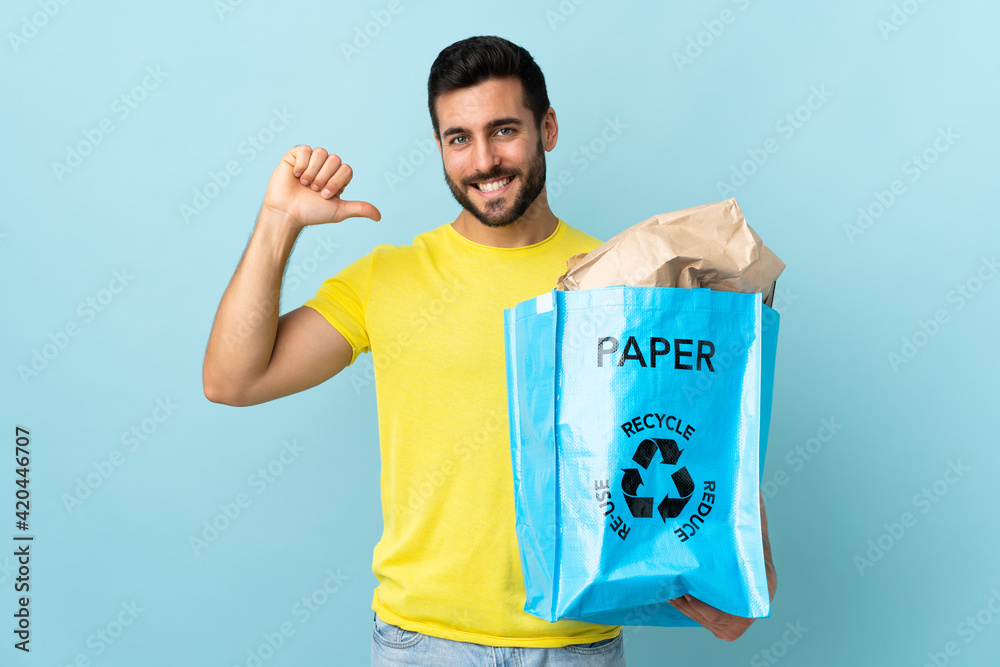 Young caucasian man holding a recycle bag isolated on blue background proud and self-satisfied Young caucasian man holding a recycle bag isolated on blue background proud and self-satisfied
