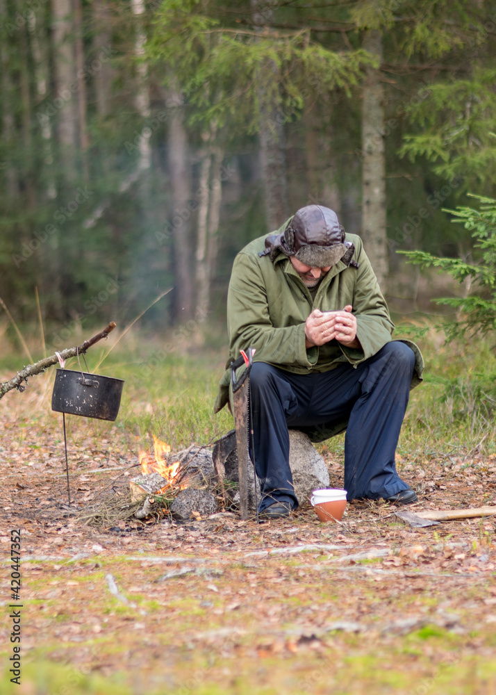 a forester in the forest drinks tea at rest, blurred forest background, bonfire with a pot over it, in the autumn a forester in the forest drinks tea at rest, blurred forest background, bonfire with a pot over it, in the autumn