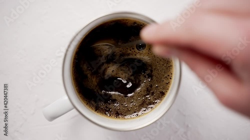 Hand stiring with a spoon a hot, black coffee in a metal mug photo