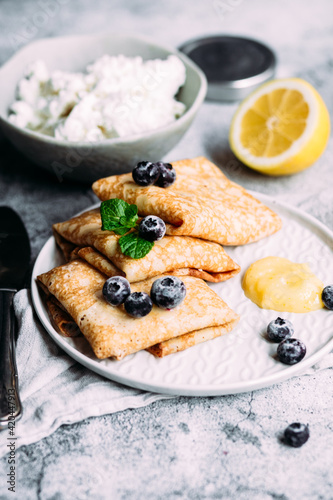 Crepes with homemade cottage cheese, blueberries and lemon curd on a gray plate