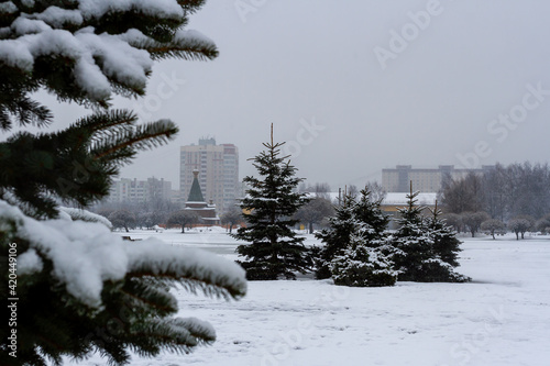 Saint-Petersburg, Russia - March 15, 2021: City park in the snow. A small church in the distance. Spruce trees. Spring snowfall in the Russian city of St. Petersburg, residential district.