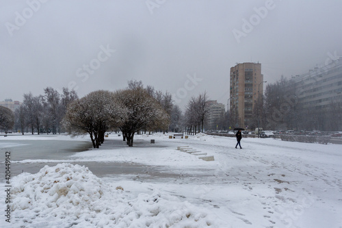 City Park. Wet snow is falling. Snow drifts. A man with an umbrella is walking in the distance. Spring snowfall in the Russian city of St. Petersburg, residential district.