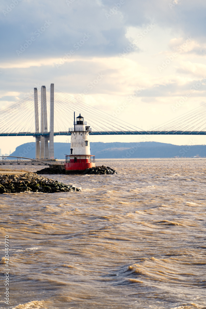 Tarrytown, NY - USA - Mar. 14, 2021: Vertical view of the Tarrytown Light, a sparkplug lighthouse on the east side of the Hudson River. Seen at sunset with the Mario M. Cuomo Bridge in the distance.