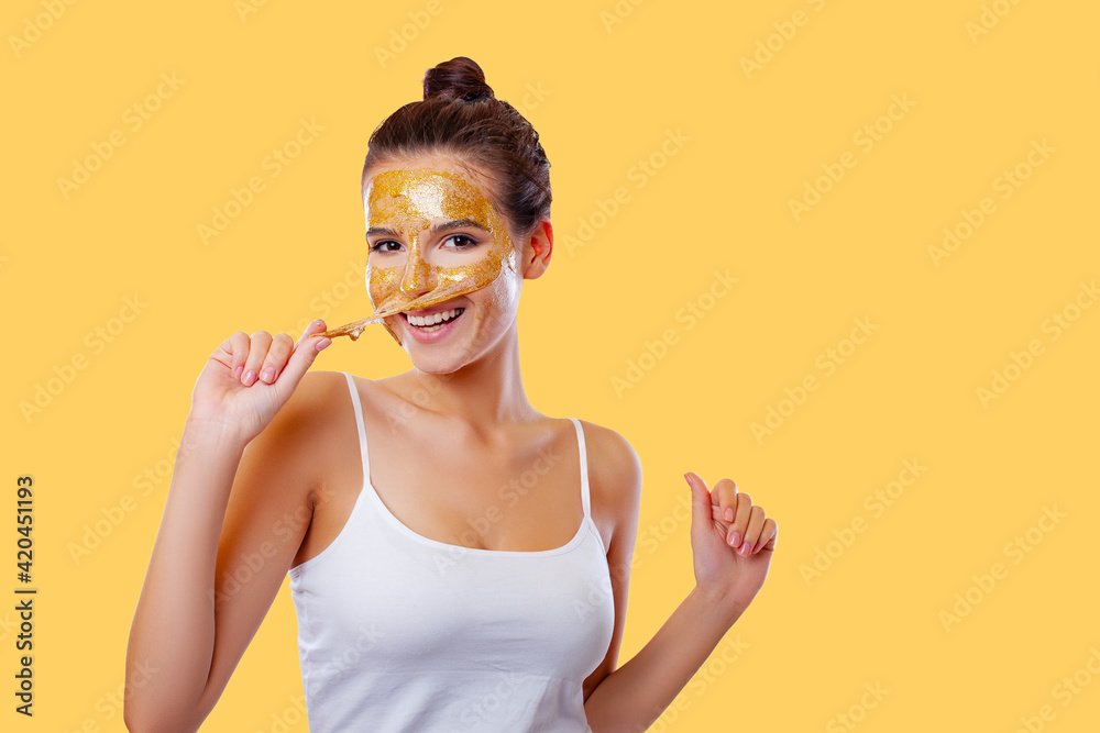Beautiful Young Woman with Clean Healthy Skin on face applies a rejuvenating mask with gold. face lifting and rejuvenation. Close-up.Cosmetology, beauty and spa therapy. colored background. Isolated. Beautiful Young Woman with Clean Healthy Skin on face applies a rejuvenating mask with gold. face lifting and rejuvenation. Close-up.Cosmetology, beauty and spa therapy. colored background. Isolated.
