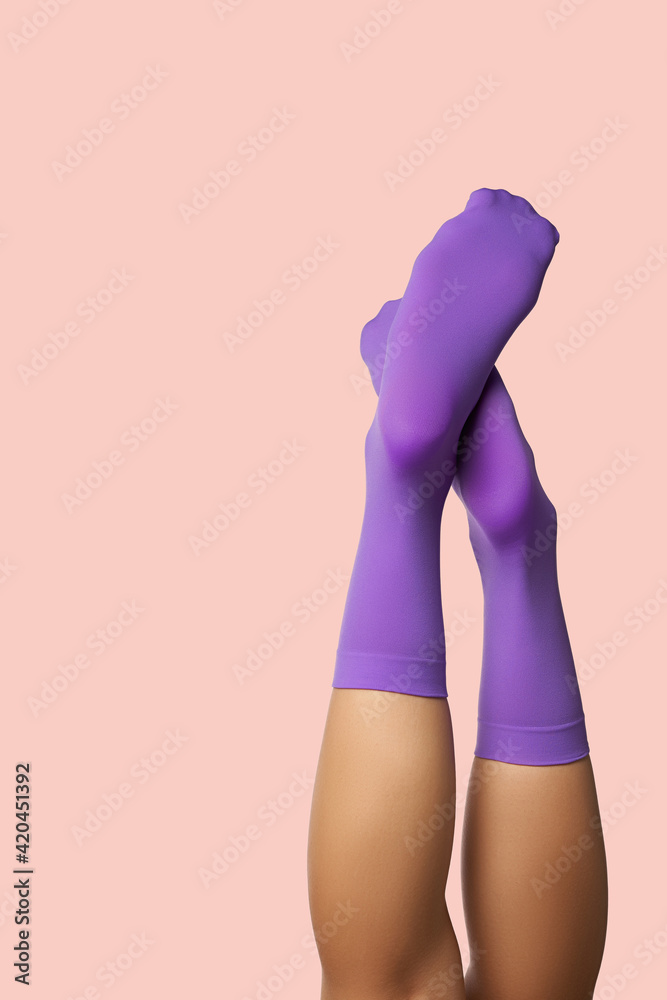 Cropped subject shot of uplifted female legs in bright shadow-proof violet socks without print. The photo is made on the pink background.