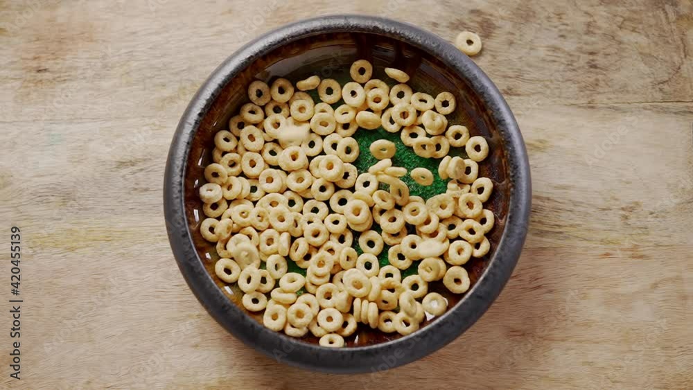 Breakfast cereal rings fall into the ceramic bowl. Placed on wooden table Breakfast cereal rings fall into the ceramic bowl. Placed on wooden table