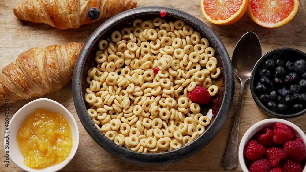 Fresh berries and pomegranate seeds fall into the ceramic bowl filled with cereal rings Fresh berries and pomegranate seeds fall into the ceramic bowl filled with cereal rings