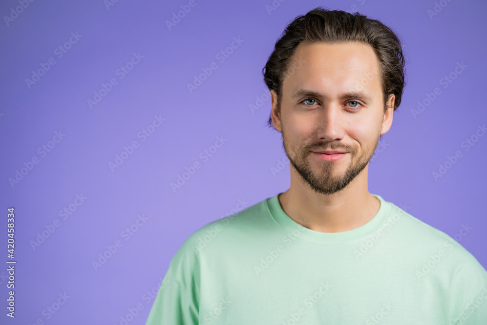 Fototapeta premium Portrait of cheerful european man looking to camera. Copy space. Young handsome kind guy smiling in studio on violet background.