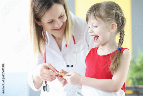 Smiling little girl with doctor pediatrician looks at transparent capsules