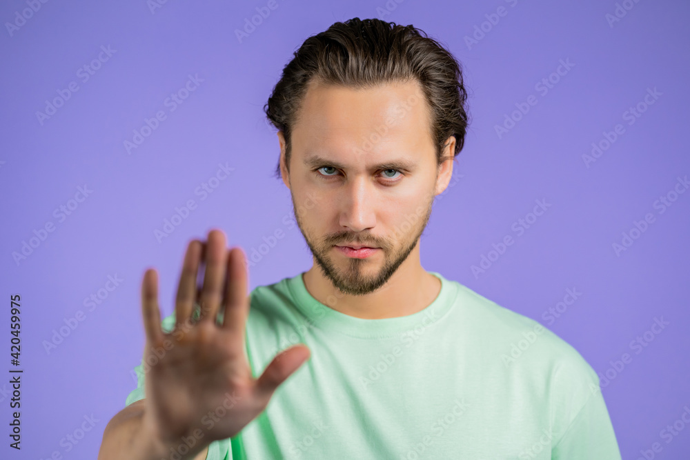 Portrait of serious man disapproving with no palm hand sign make basta, negation, enough gesture. Denying, Rejecting, Disagree. Portrait of handsome guy on violet background Portrait of serious man disapproving with no palm hand sign make basta, negation, enough gesture. Denying, Rejecting, Disagree. Portrait of handsome guy on violet background