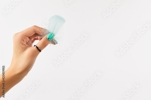 Well-groomed female hand holding feather on white background