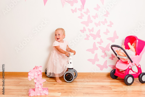 blonde one-year-old girl rides jogger at home. one year old photo