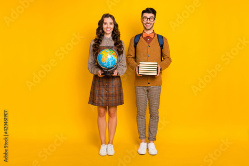 Full body photo of brunette couple wear plaid dress pants bow-tie hold books globe isolated on yellow color background