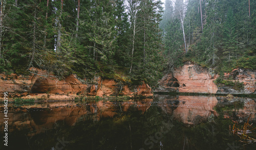 Sandstone cliffs and a beautiful evergreen forest by the Brasla river in Latvia during cloudy day photo
