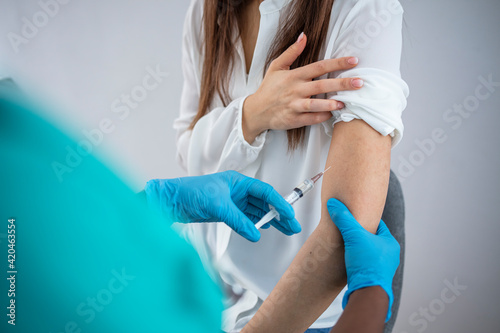 Female doctor holding syringe making covid 19 vaccination injection dose in shoulder of female patient wearing mask
