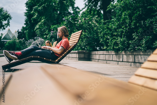 Man lying on deck chair and using laptop in park Fototapete