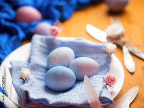 Naturally colored stylish Easter eggs in a plate, decorative flowers, on a wooden table