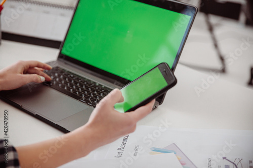 Female hand holding mobile with green screen.Mobile laptop workplace