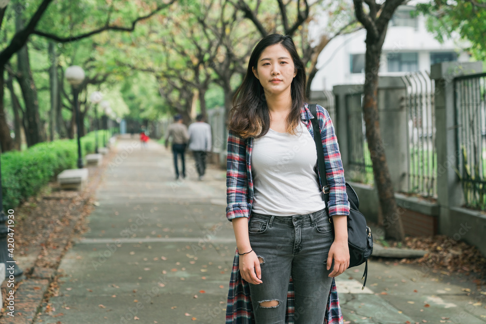 Young beautiful stylish asian chinese woman in summer wears walking between trees at alley. charming girl standing on pathway surrounding by nature fresh in spring. female face camera with bag. Young beautiful stylish asian chinese woman in summer wears walking between trees at alley. charming girl standing on pathway surrounding by nature fresh in spring. female face camera with bag.