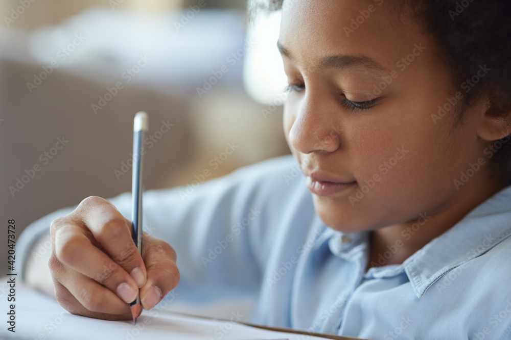 Close up shot of mixed race teen girl looking focused, writing with a pencil while doing homework, spending time at home Close up shot of mixed race teen girl looking focused, writing with a pencil while doing homework, spending time at home