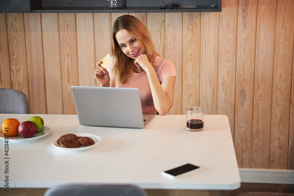 Charming woman holding credit card and using laptop at home Charming woman holding credit card and using laptop at home