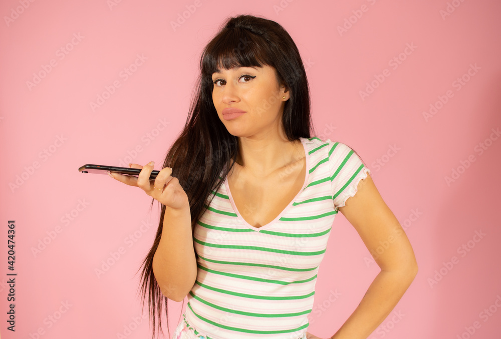 Happy beautiful young woman with long hair holding mobile phone over pink background Happy beautiful young woman with long hair holding mobile phone over pink background