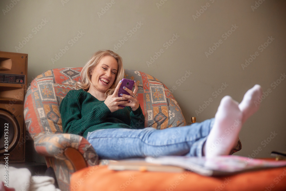 Obraz premium one young really happy woman laughing, cracking a smile, sitting in sofa, while texting on her smart phone.
