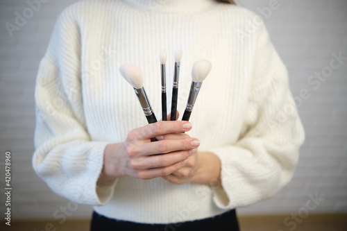The girl holds brushes in her hands for makeup. In a white sweater  white brushes  on a black background. Soft selective focus.