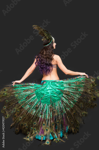 Dancer holds peacock feathers in her hands black background view from the back.