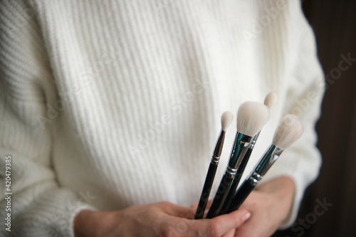 The girl holds brushes in her hands for makeup. In a white sweater, white brushes, on a black background. Soft selective focus.
