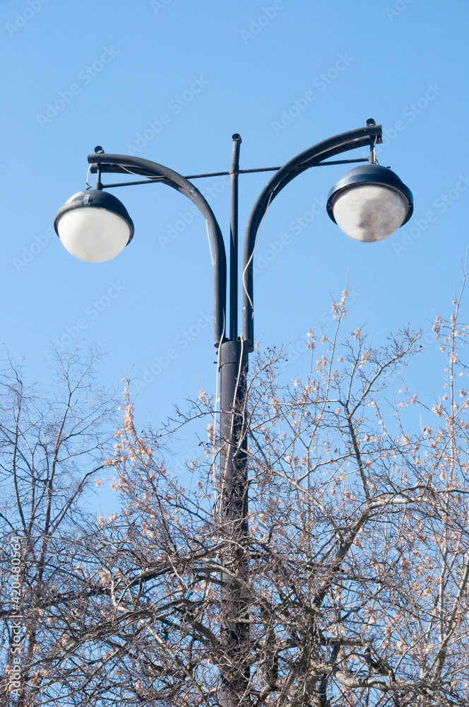 Lighting pole with lamps against the blue sky and tree branches. Lighting pole with lamps against the blue sky and tree branches.