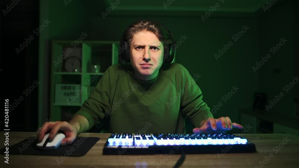 Upset gamer in a headset cries after a loss, sitting at night in a bedroom with a purple light. An emotional gamer in despair cries after losing. Upset gamer in a headset cries after a loss, sitting at night in a bedroom with a purple light. An emotional gamer in despair cries after losing.