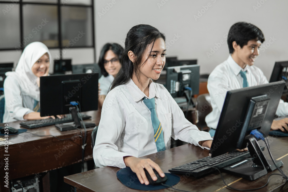 Indonesian female high school students smile while using a computer PC with their friends studying in a computer practice room at school Indonesian female high school students smile while using a computer PC with their friends studying in a computer practice room at school
