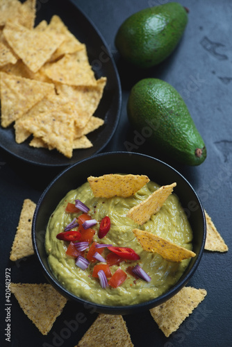 Guacamole dip served with corn chips over black stone background, vertical shot, elevated view