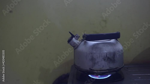 Metal colored kettle with boiling water on a stove in poor kitchen photo