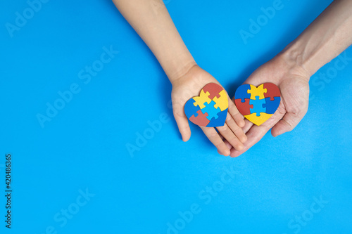 Father and autistic son hands holding jigsaw puzzle heart shape. Autism spectrum disorder family support concept. World Autism Awareness Day