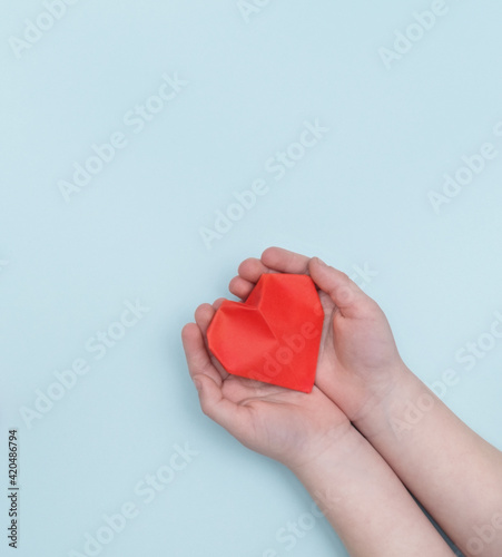 a small child holds a red paper three-dimensional heart on a blue background. Top view. valentine s day. Mother s Day. The concept of love and education. World Health Day. Copy The Space.