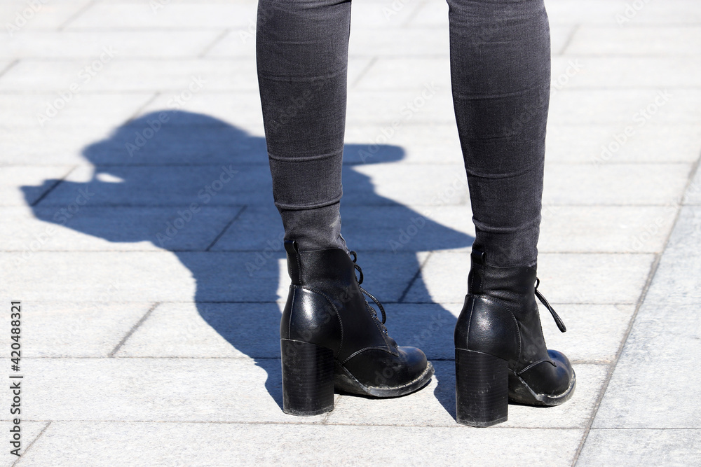 Female legs in black jeans and boots on high heels on the street, shadow on pavement. Female fashion in spring, ladies footwear and clothing