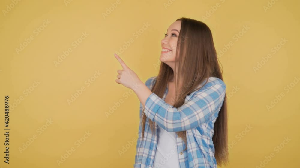 Young woman student shows index finger aside on yellow background Young woman student shows index finger aside on yellow background