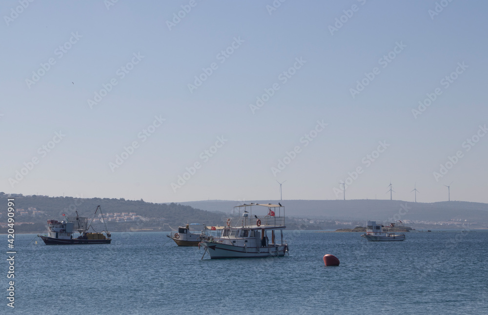 fishing boats moored in the mediterranean sea and hills, houses, forest and wind farms in the background. Concept of tranquility