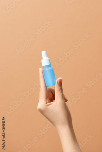 Hands hold serum collagen moisturizer of face into clear blue bottle soft light photo
