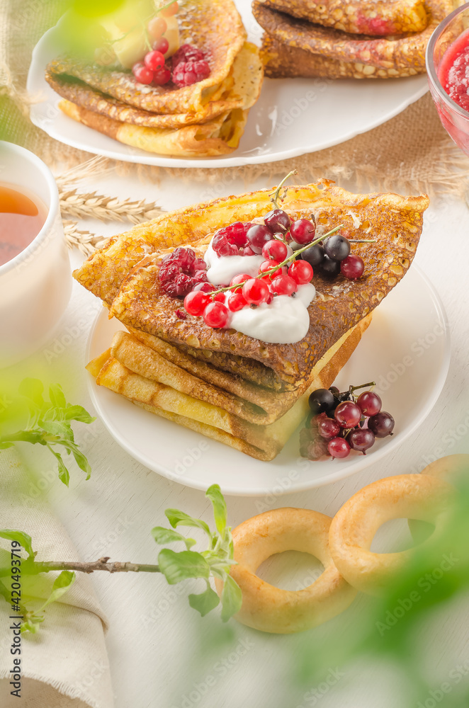 Pancakes with berries and sour cream for the Russian Maslenitsa holiday on a white background with bokeh of greens Pancakes with berries and sour cream for the Russian Maslenitsa holiday on a white background with bokeh of greens