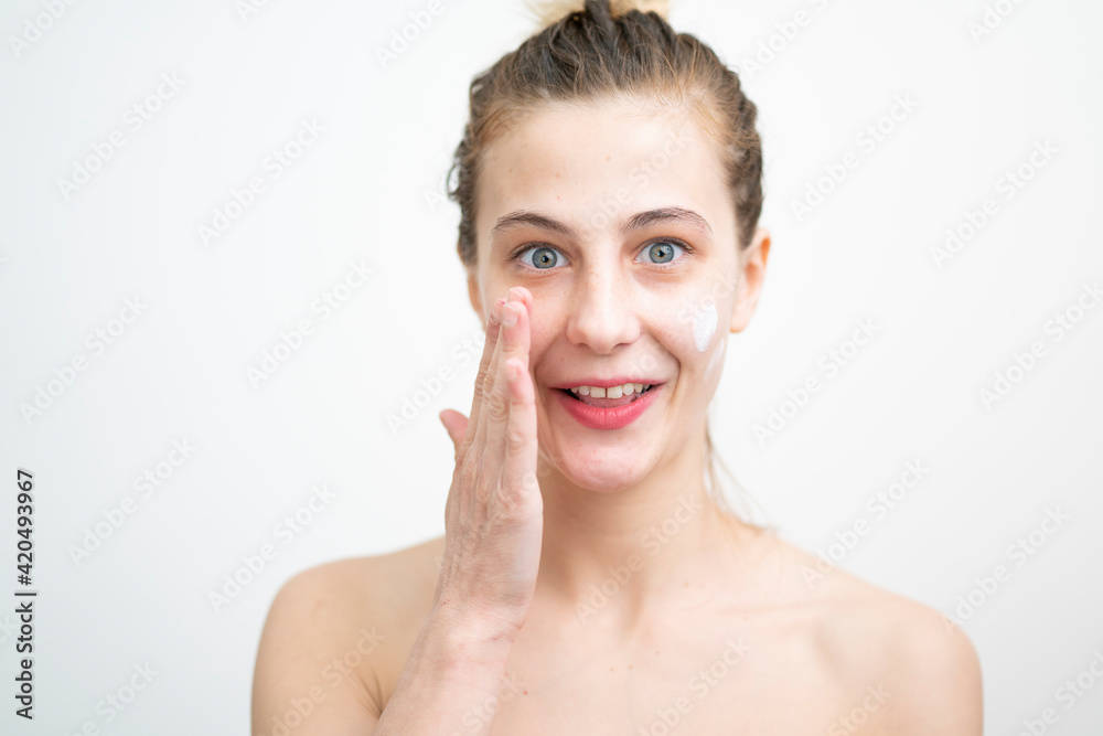 Happy Young Woman Applying Cream on Her Face, Studio Shot on White Background Happy Young Woman Applying Cream on Her Face, Studio Shot on White Background