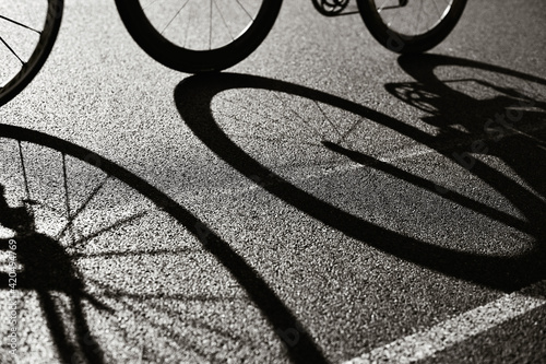 Road Cycling Racing Bike Abstract backlit view of shadow bicycle wheel racing along road in bicycle lane. Silhouette of front and rear road bike on a bright modern pavement