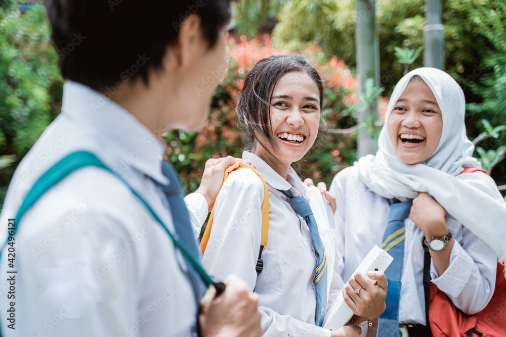 two female high school students and a boy wearing school bags and smiling together while chatting in the schoolyard