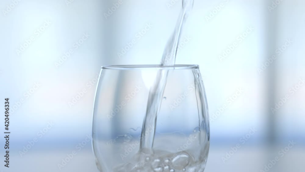 A transparent glass of water is placed on the table and a water bottle is poured into the glass in the house on a white background. A transparent glass of water is placed on the table and a water bottle is poured into the glass in the house on a white background.