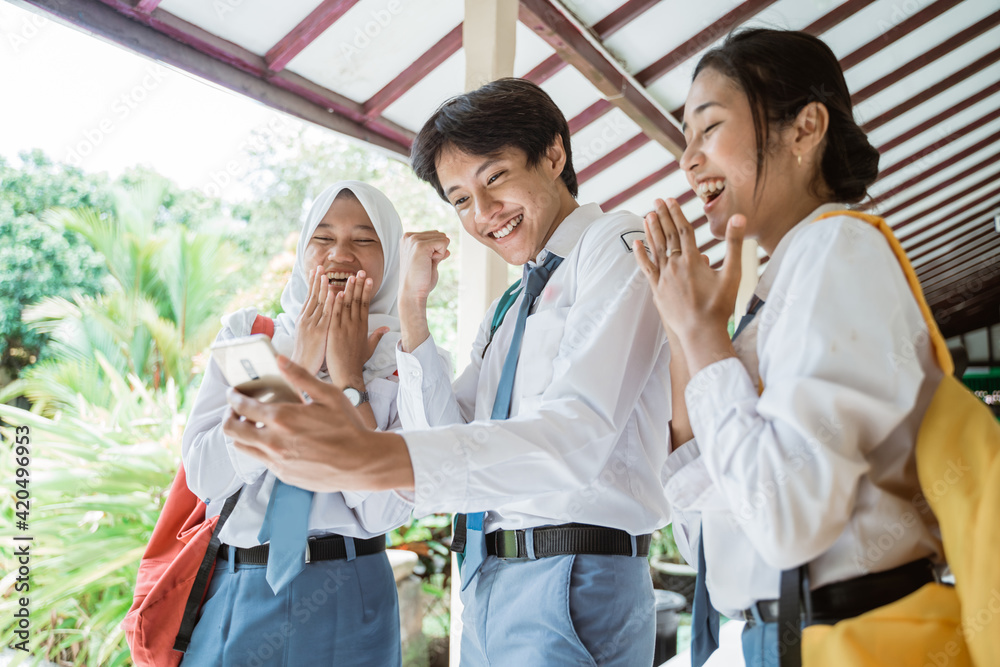 Obraz premium three Indonesian high school students look at the screen using one smartphone to see the announcement of graduation together at school